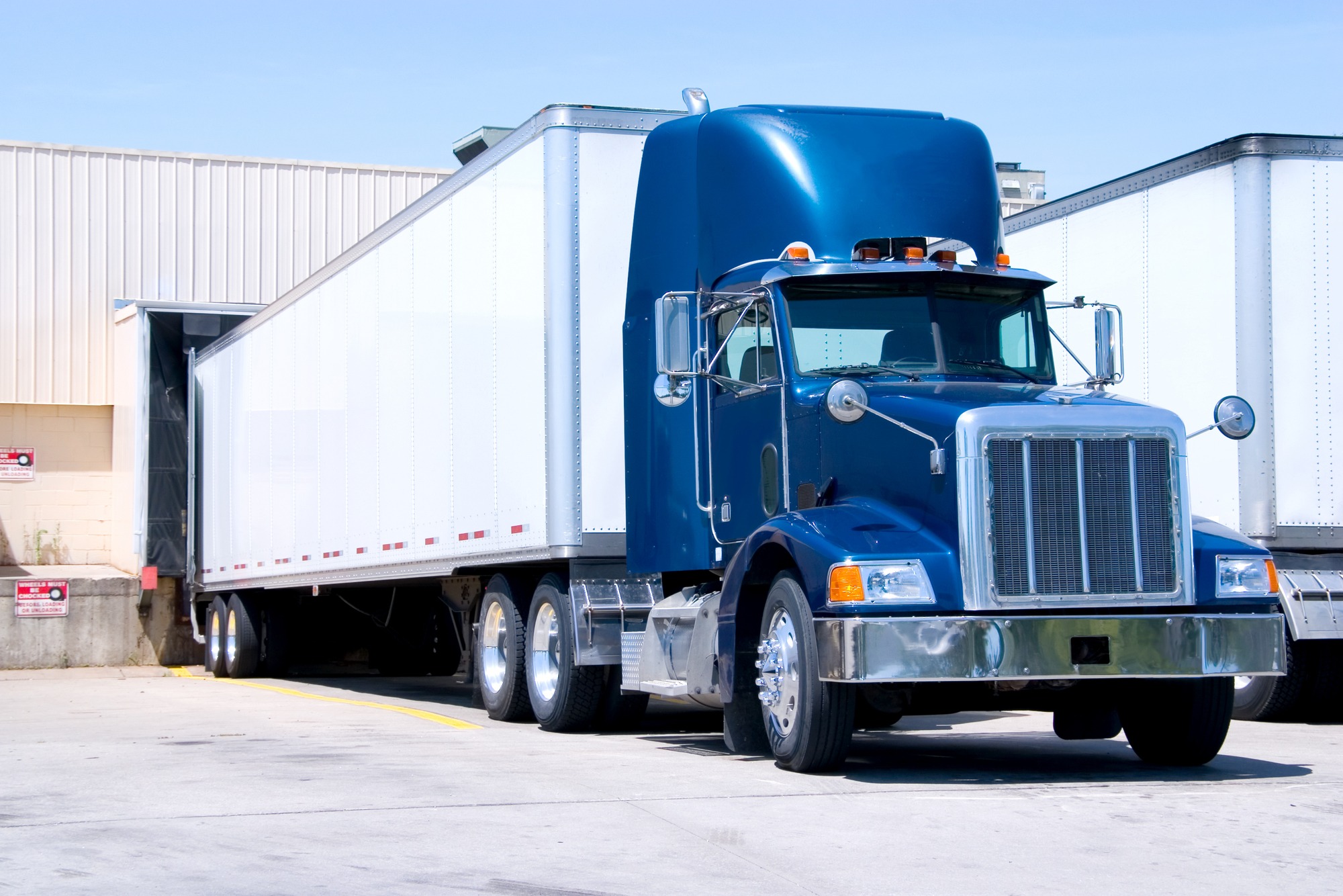 Blue semi-truck parked at a loading dock, ready for unloading or loading goods. The image highlights the trucking industry and logistics operations.